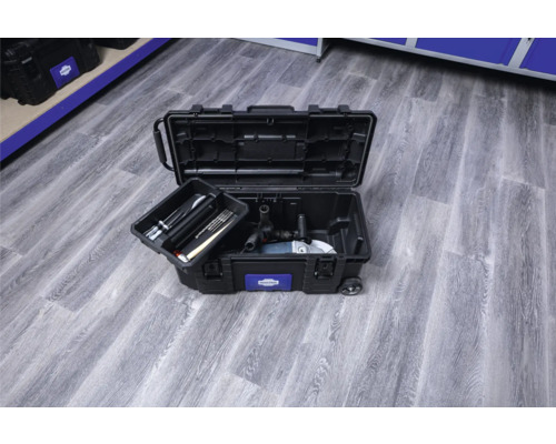 Öppen svart verktygslåda med verktyg på ett trägolv