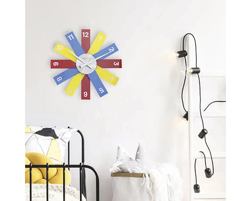 Scen med en väggklocka med färgglada urtavlor, en stege med glödlampor och en säng.