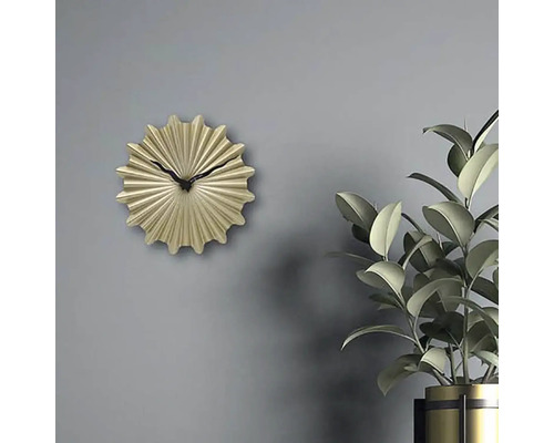 Dekorativt guldfärgad väggklocka med svart visare bredvid krukväxt