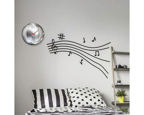 Väggdekoration med spegelbollsur och väggdekal med musiknotlinjer ovanför en säng.