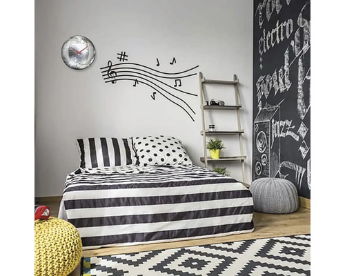 Sovrum med sängkläder med randigt mönster, väggdekal med noter och väggklocka med spegelbollar