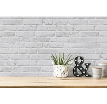 Dekorativ rumsdesign med tegelstapeter, växt, ''&''-symbol och behållare på ett träbord.