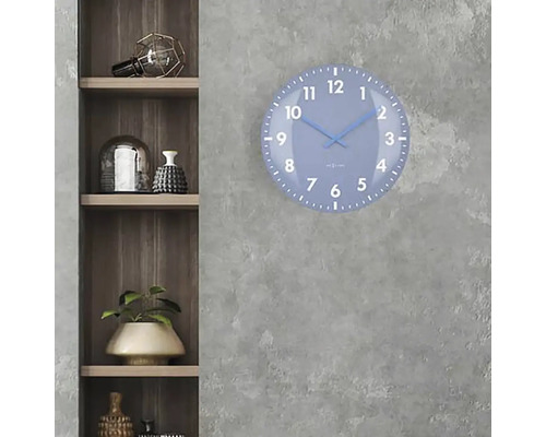 En blå väggklocka med urtavla hänger på en grå vägg bredvid en trähylla.