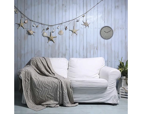 Vardagsrum med vit soffa, stickad pläd, väggklocka samt dekoration med snäckor och sjöstjärnor