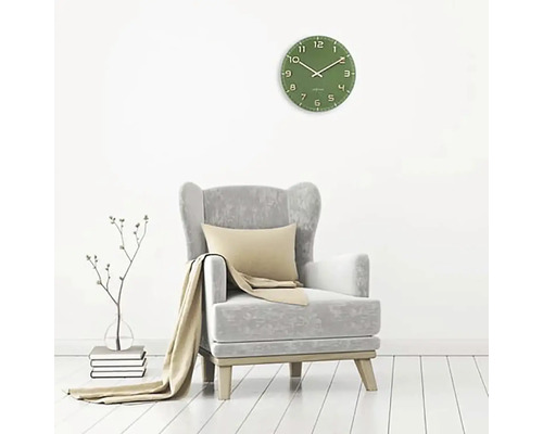 Vardagsrum med grön väggklocka, fåtölj, kudde och filt.