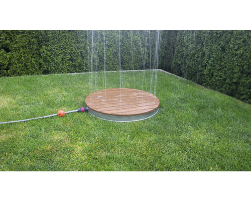 Rund grässpridare av trä och metall på en gräsmatta i trädgården.