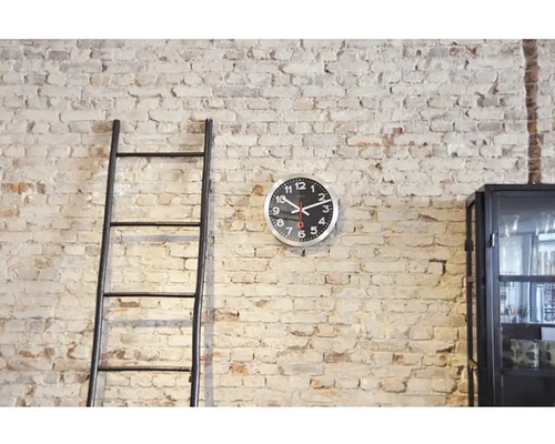 Miljöbild med stege, väggklocka och skåp framför en tegelvägg