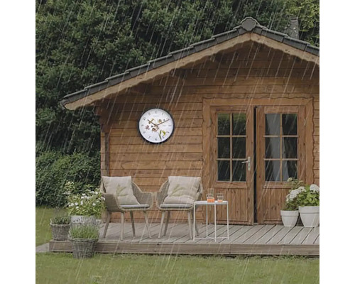 Scen med trädgårdshus, trädgårdsmöbler och en väggklocka i regnet.