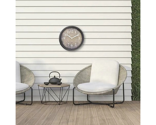 Scen med utomhusklocka, stolar och ett litet bord med tekanna