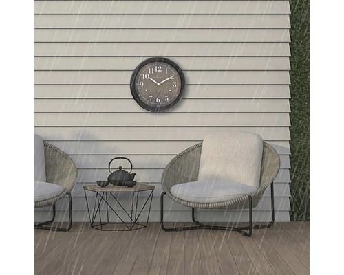 Scen med en väggklocka, två stolar och ett bord utomhus i regnet.