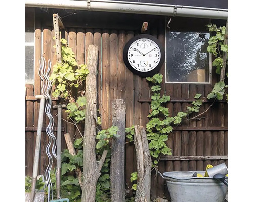 Utomhusscen med väggklocka, vinranka, trädgårdsredskap och trästaket