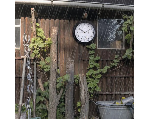 Trädgårdsscen med en väderbeständig utomhusklocka på en trävägg i regnet.