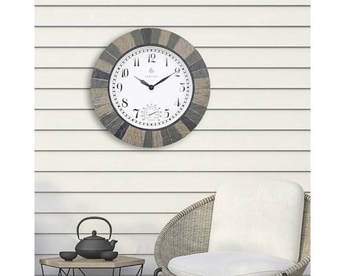 Utomhusklocka med termometer på en vägg ovanför en stol och ett bord.