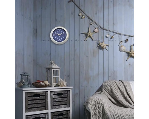 Dekorativt vardagsrum med väggklocka, byrå, lykta, soffa och maritima dekorativa element som sjöstjärnor och snäckor.