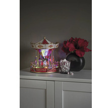 Dekorativ karusell med belysning, bredvid ett glas marshmallows och en vas med blommor på ett skåp