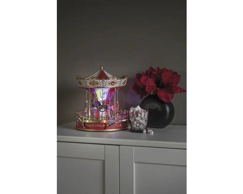 Dekorativ karusell med belysning, bredvid ett glas marshmallows och en vas med blommor på ett skåp