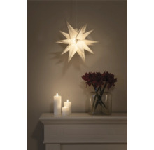 Juldekoration med upplyst pappersstjärna, ljus och blommor i vas på spiselkransen