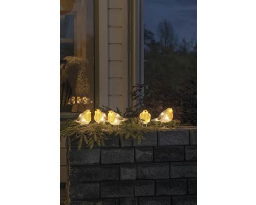 Dekorativa upplysta rödhakefigurer på en mur med grangrenar