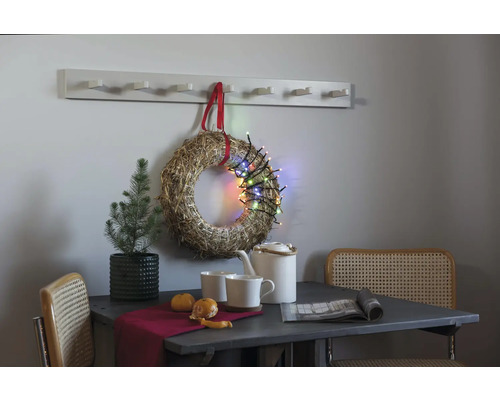 Dekorativt stilleben med bord, stolar, krans, ljusslinga och hatthylla