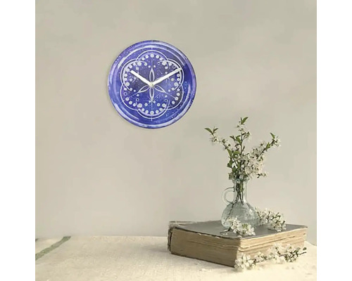Väggklocka med blått mönster och vita visare bredvid en blomvas