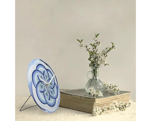 Bordsklocka med blått blommönster på en bok bredvid en vas med blommor