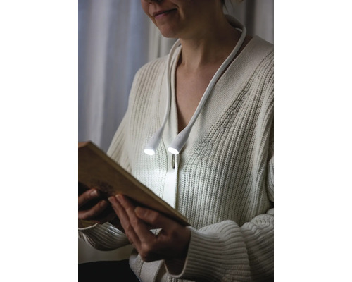 En person läser en bok med en nacklampa.