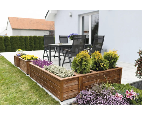 Träplanteringslådor med olika växter i trädgården och utemöbler i bakgrunden.