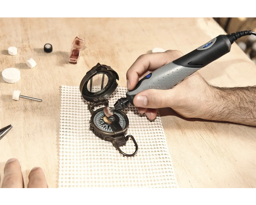 Hand som polerar en kompass med ett Dremel-verktyg på en träyta