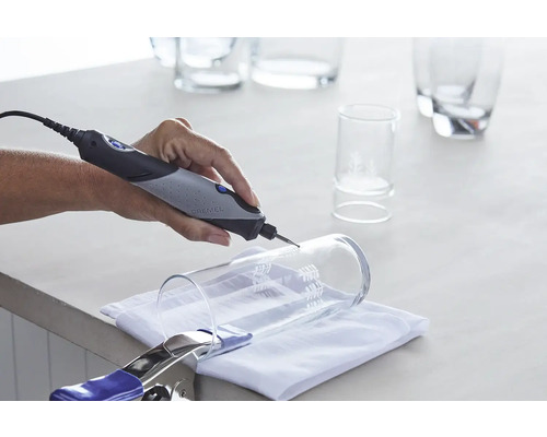 Dremel logotyp. Hand slipar ett glas med ett Dremel multifunktionsverktyg. Glaset är fastsatt med en klämma.