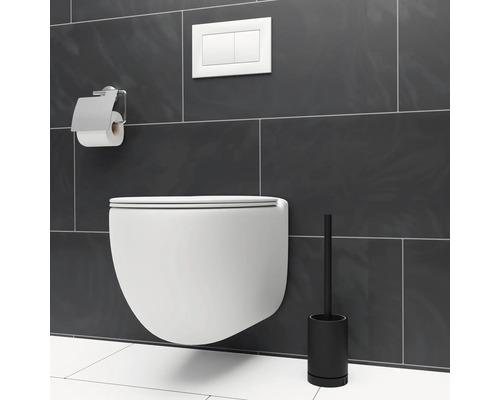 Vägghängd toalett med toalettpappershållare och toalettborste framför en grå vägg