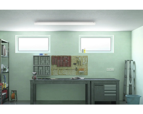 Verkstad med arbetsbänk, verktygsvägg och hyllor under en taklampa.