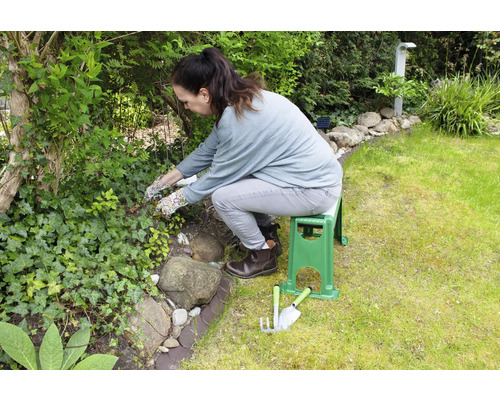 En kvinna arbetar i trädgården med en trädgårdsbänk och trädgårdsredskap.