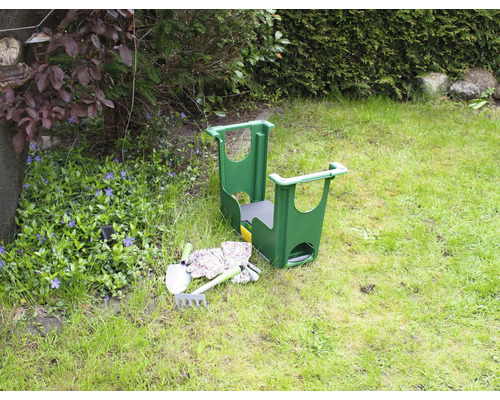 Trädgårdsscen med en trädgårdspall, en spade, en kratta och trädgårdshandskar på en gräsmatta