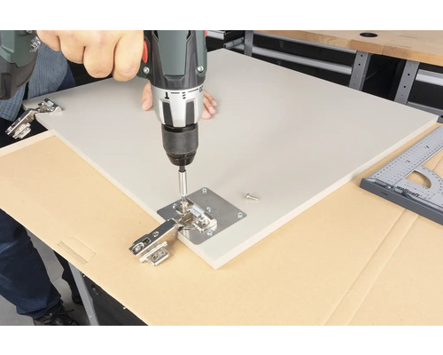 En man fäster ett gångjärn med en sladdlös skruvdragare på en platta.