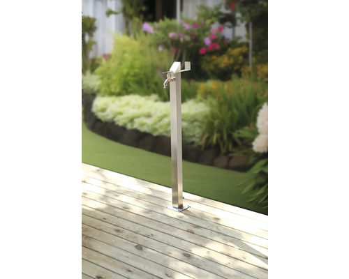 Trädgårdstappkran i metall på trädäck med trädgård i bakgrunden