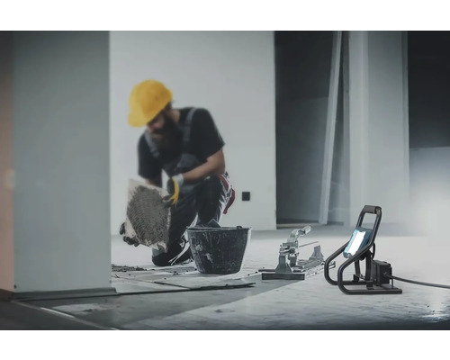 Plattsättare som arbetar med hink, kakelskärare och byggstrålkastare