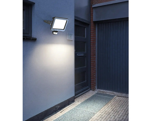 Utomhusbild av en upplyst LED-utomhuslampa med rörelsedetektor på en husvägg