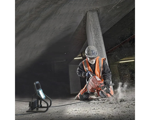 En byggnadsarbetare använder en bilningshammare i en betonggrop, upplyst av en arbetslampa.