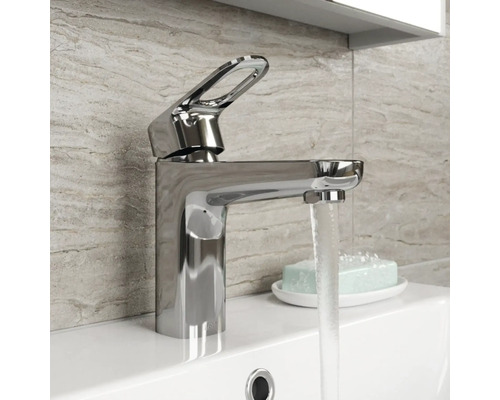 Blank tvättställsblandare i metall på ett handfat med rinnande vatten