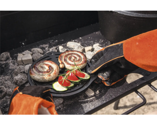 Två spiralformade korvar och grönsaker på ett grillgaller med grillvante