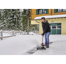 En man använder en snöslunga framför ett hus på vintern.