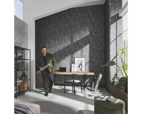 Vardagsrum med mönstrad tapet, skrivbord och man med tapetrulle