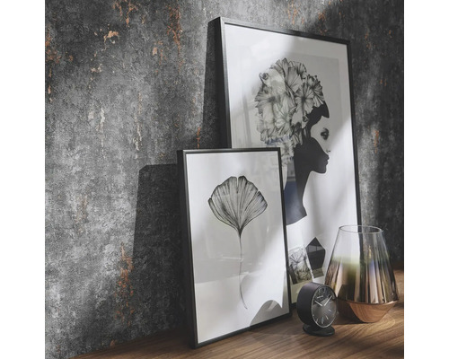 Dekorativ scen med två inramade bilder, en klocka och en vas på en hylla framför en strukturerad vägg.