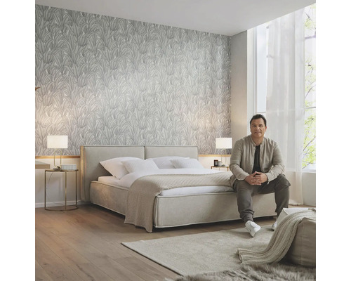 Ljust sovrum med mönstrad tapet, dubbelsäng, matta och sittande man