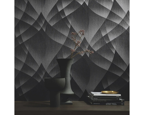 Interiörbild av ett rum med mönstrad tapet, böcker och vaser på ett bord.