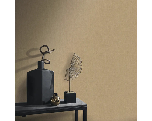 Dekorativ scen med en strukturerad tapet, kompletterad med en svart vas, en gyllene sfär och en fläktformad metallskulptur på ett bord.