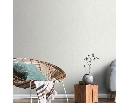 Ljust vardagsrum med rottingfåtölj, träbord och diskret mönstrad tapet.