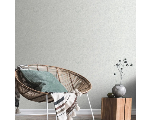 Vardagsrum med rottingfåtölj, kudde, filt och sidobord i trä med dekoration framför en strukturtapet