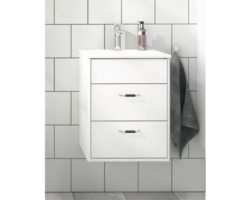 Vitt tvättställsskåp med tre lådor, armatur och handduk i badrummet.