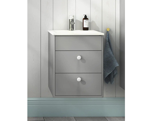 Grått tvättställsskåp med tre lådor, tvättställsskiva, armatur, tvålpump och handduk på väggen